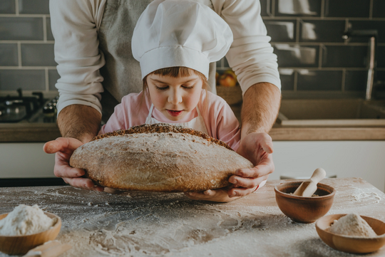 Kind mit Bäckerhaube riecht an einem frisch gebackenen Brot