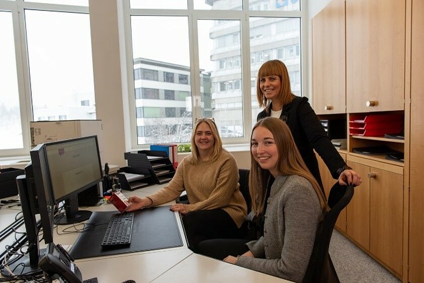 Drei lächelnde Frauen in einem Büro kümmern sich um die Anliegen der Kunden